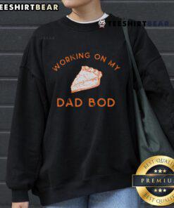Cozy sweatshirt with 'Working on my dad bod' graphic, paired with a delicious pie for two on a dining table.