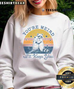 Alt Text: Cute 'Youre Weird, Ill Keep You' sweatshirt against a vibrant sunset backdrop, perfect for cozy casual wear.
