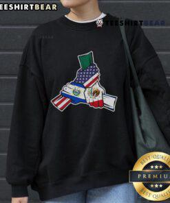 Couple holding hands wearing 'Roots' sweatshirt featuring Mexico, El Salvador, and USA flags, symbolizing unity.