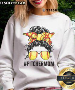 Softball mom in a messy bun wearing a 'Nice Softball Pitcher Mom' sweatshirt, cheering at a game.