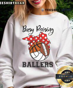 Alt Text: Official Busy Raising Ballers sweatshirt featuring volleyball, football, and basketball designs in a stylish layout.
