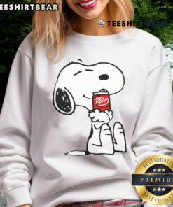 Cute Snoopy hugs a Dr Pepper bottle on a cozy sweatshirt, perfect for fans of Peanuts and soda lovers.
