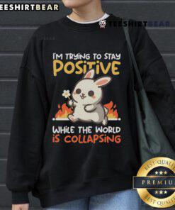 Cute bunny on a sweatshirt with the phrase I'm trying to stay positive while the world is collapsing. Perfect for cozy vibes.