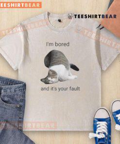 Alt Text: Funny cat looking bored in a washed t-shirt, playfully blaming its owner for the lack of fun activities.