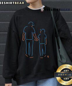Father and son wearing Happy New York Mets neon sweatshirts, showcasing team spirit and family bonding at a game.