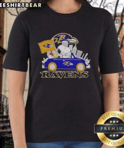 Alt Text: Snoopy and Woodstock driving a car with Baltimore Ravens skyline in the background on a ladies tee.