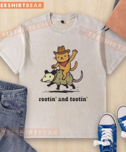 Alt Text: Top Cowboy Orange Cat riding an opossum on a Rotin and Tootin washed t-shirt, showcasing playful animal art.