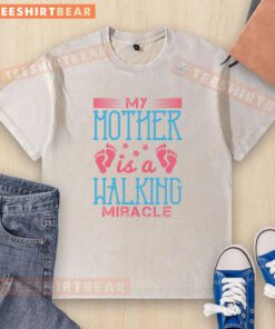 Alt Text: Good My Mother Is A Walking Miracle washed t-shirt displayed on a hanger, featuring a bold inspirational graphic design.