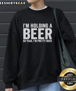 Person wearing an 'Awesome I'm Holding A Beer' sweatshirt, smiling and enjoying a casual moment with a drink.