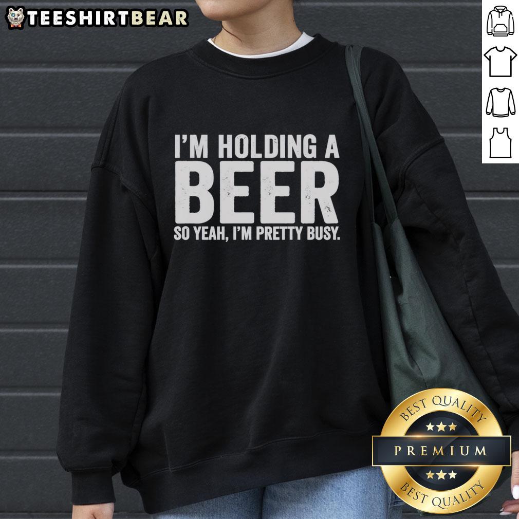Person wearing an 'Awesome I'm Holding A Beer' sweatshirt, smiling and enjoying a casual moment with a drink.