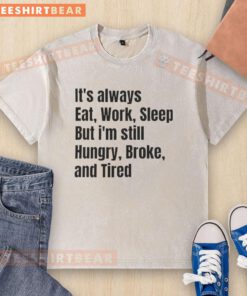 Top 'It's Always Eat Work Sleep But I'm Still Hungry Broke And Tired' washed t-shirt displayed on a wooden table.